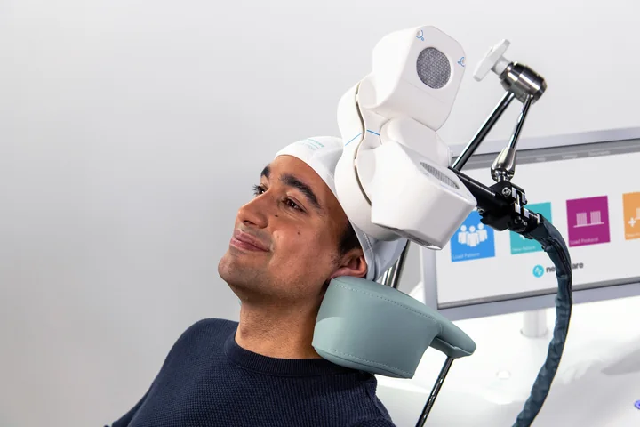 Close view of an Apollo magnetic coil resting beside a seated person’s scalp
