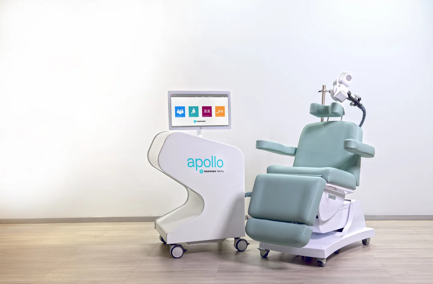 Apollo TMS system beside a mint-colored treatment chair, with a coil positioned above the headrest