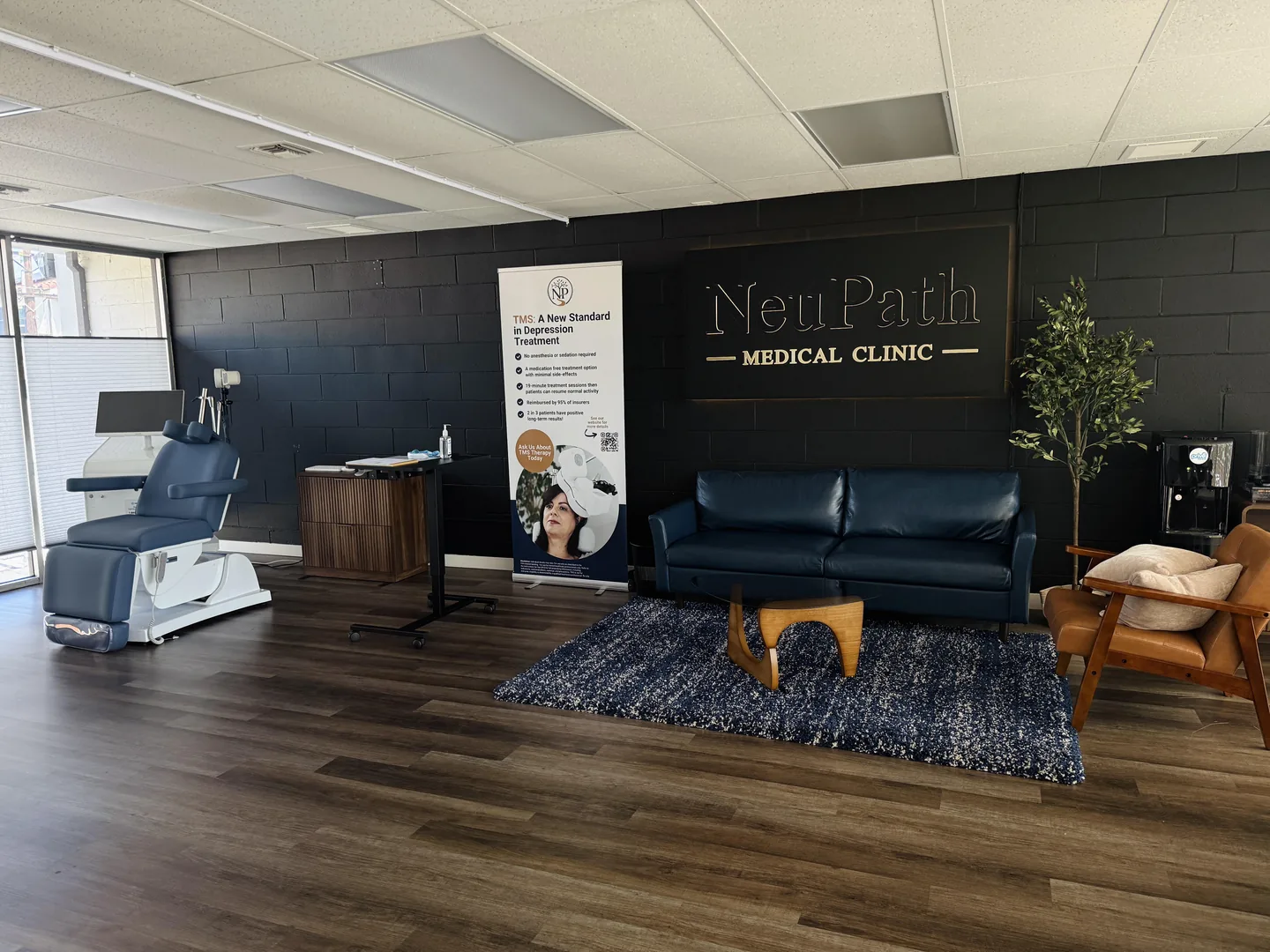 Inside NeuPath in Long Beach: navy seating, warm wood floors, plants and the clinic sign beside a sunlit window