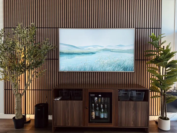 A calm landscape on a framed screen set into a slatted wood wall, with plants and a refreshment cabinet